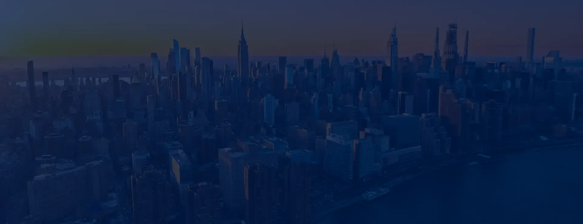 A panoramic view of a city skyline at dusk, showcasing tall skyscrapers, including the Empire State Building, against a twilight sky.